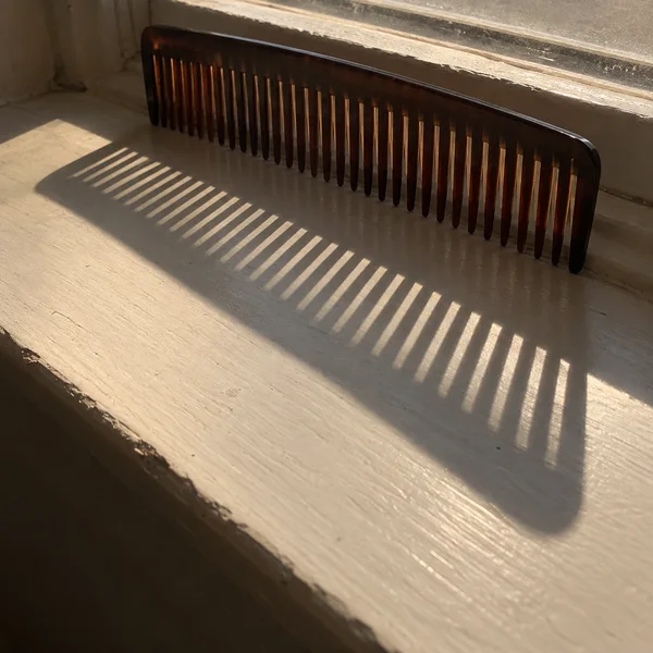 A dark brown comb leans against a bathroom window frame above a cream-painted wooden sill.