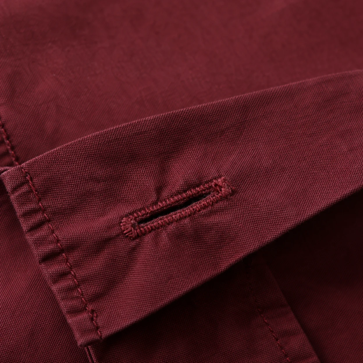 A close-up of a burgundy shirt cuff with a diagonally oriented buttonhole, raised stitching and visible fabric seams.