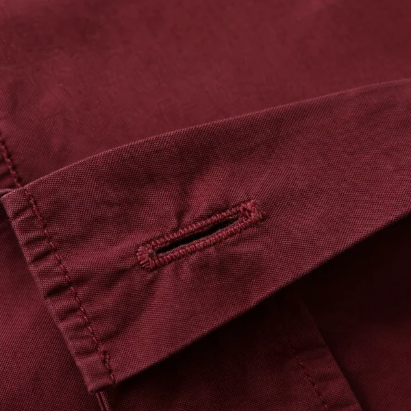 A close-up of a burgundy shirt cuff with a diagonally oriented buttonhole, raised stitching and visible fabric seams.