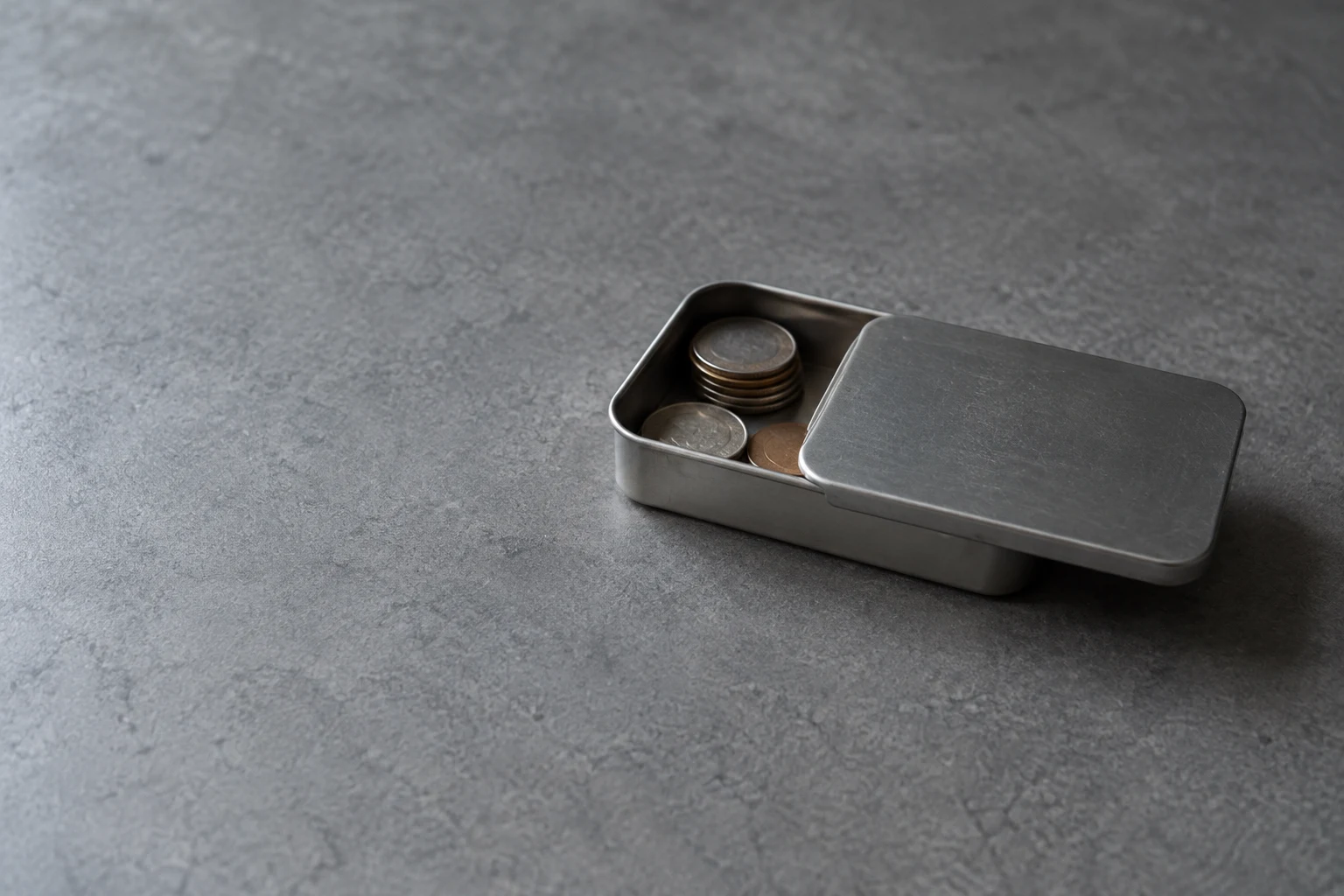 A small unbranded steel tin with its sliding lid partly open sits on a textured grey tabletop.
