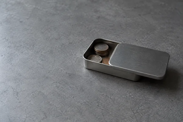 A small unbranded steel tin with its sliding lid partly open sits on a textured grey tabletop.