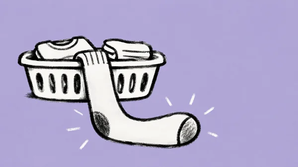 A large white sock with a rounded toe and dark heel patch drapes over the front of a laundry basket.