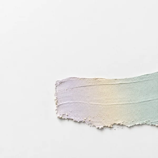 A textured horizontal sweep of lilac, pale gold and mint plaster crosses the lower-right of a chalk-white field, with a rough scraped edge and soft shadow.