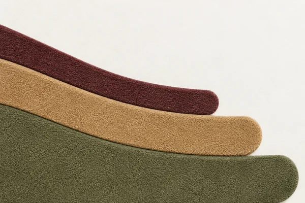 Three plush, curved textile bands in dusty burgundy, warm camel and moss green sweep diagonally across a chalk-white background, with large open space above…