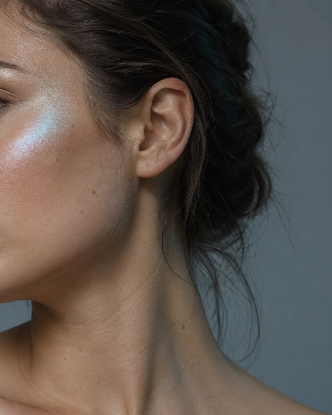 Close studio crop of an adult model’s cheek, ear, jaw and neck, with dark hair pulled back.