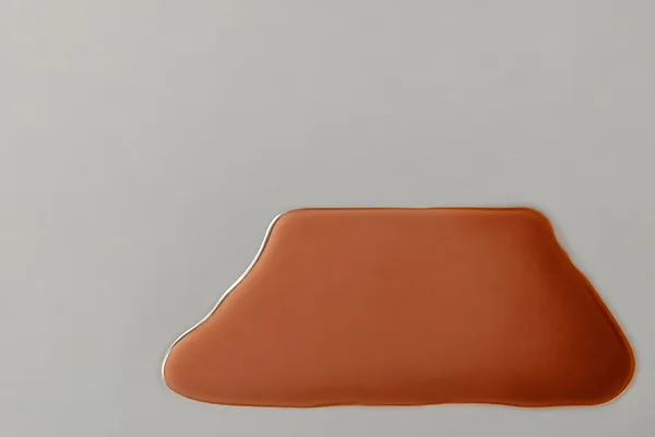 An overhead abstract composition shows a broad terracotta-colored liquid pool with a nearly straight upper edge and rounded, sloping sides in a smooth…