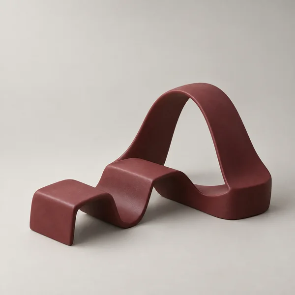 A thick oxblood ribbon sculpture with two low folds and a tall asymmetric arch sits on a seamless warm-grey ground, lit softly from the upper left.
