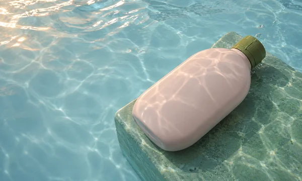 A blank shell-pink refill bottle with a moss-green screw cap lies diagonally on a green stone-like platform underwater, with warm caustic reflections across…