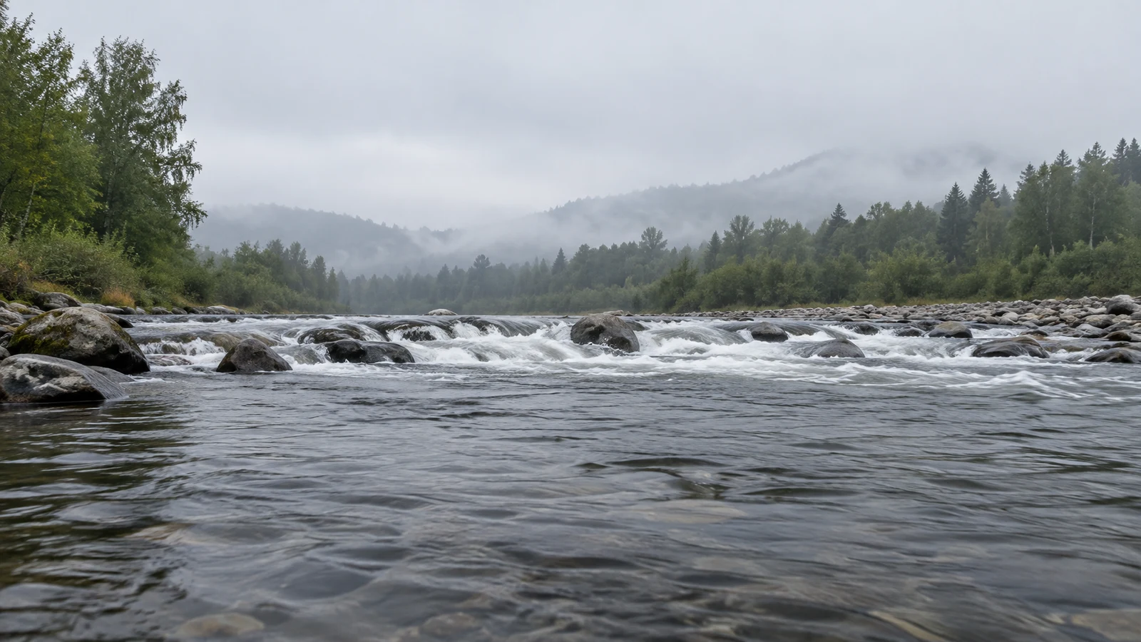 A broad river flows toward the camera over rounded rocks, forming a horizontal band of white rapids.