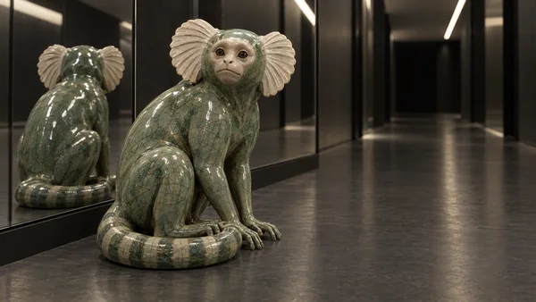 A glossy green ceramic marmoset sculpture with ivory fan-shaped ears and a curled tail sits on a dark floor beside its reflection in a mirrored hallway.