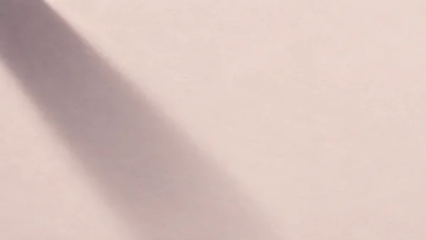 A broad, soft-edged violet-grey shadow falls diagonally across a pale blush, finely textured surface, leaving open space on the right.
