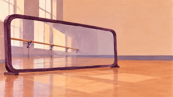 A wide, low aubergine-framed freestanding mirror stands on a peach studio floor, reflecting a ballet barre, tall windows and pale light; open peach wall fills…