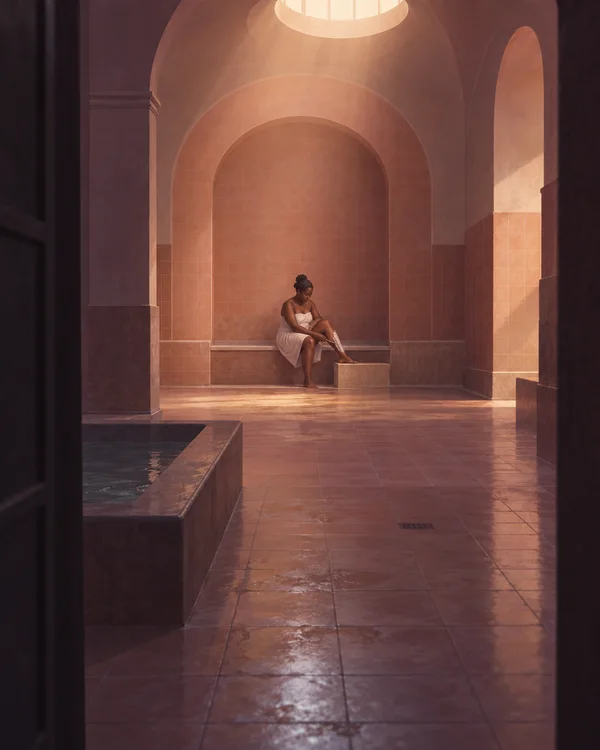 A Black woman in a white bath wrap sits on a built-in bench in a tall coral-tiled bathing room, leaning over one raised leg; a shallow pool occupies the left…