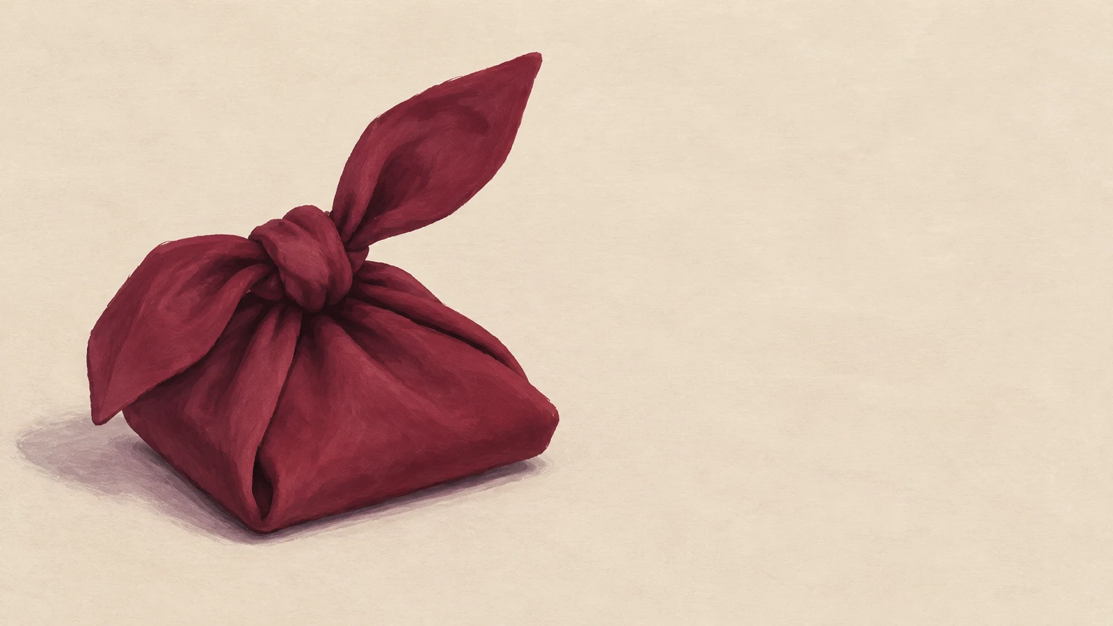 A burgundy cloth tied into a large knot rests on a pale beige surface, with a soft shadow and open space to the right.