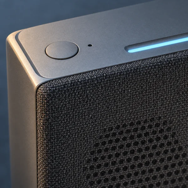 Extreme close-up of a charcoal fabric-covered smart speaker with a satin-metal top, one round button, a small aperture and a narrow blue illuminated strip…