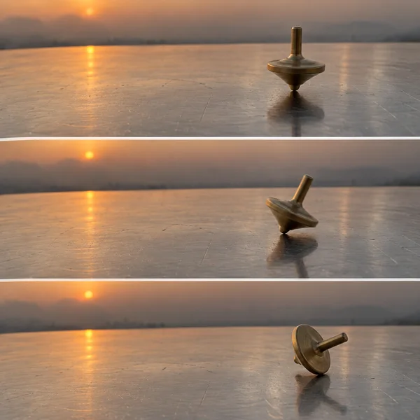 Three horizontal photographs show a brass spinning top on a reflective metal tabletop at sunset: upright in the first, leaning in the second, and on its side…