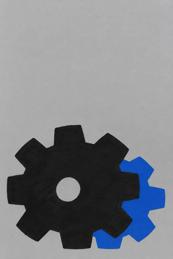 A large, roughly cut black gear with a small circular opening sits low against a textured silver-grey background.