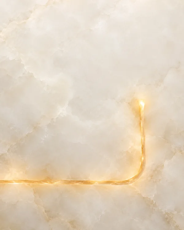 A warm ivory mineral-textured abstract surface with a glowing amber channel entering from the lower left, running horizontally across the lower area, then…