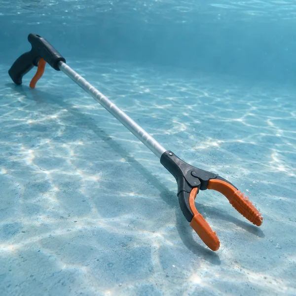 A dark-handled litter picker with a satin-silver shaft and orange gripping jaws rests diagonally on a pale blue underwater floor; the open jaws sit in the…