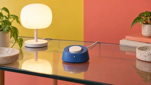 A low cobalt-blue device with a large ivory dial and a small amber light sits near the center of a reflective glass table.