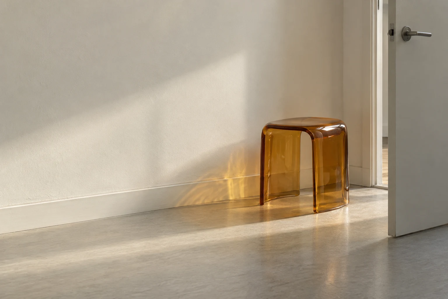 A translucent amber resin stool stands beside a partly open door in a quiet room with an off-white wall, baseboard and pale grey floor.