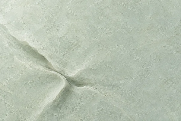 A pale celadon-green stone-like surface with mottled mineral grain and broad, soft-shadowed folds converging left of centre; the upper and right areas are…