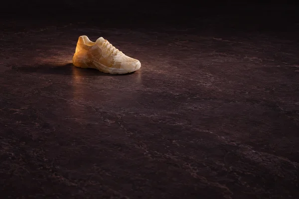 A translucent amber-toned carved sneaker rests on a dark aubergine stone surface, with ample empty space around it.