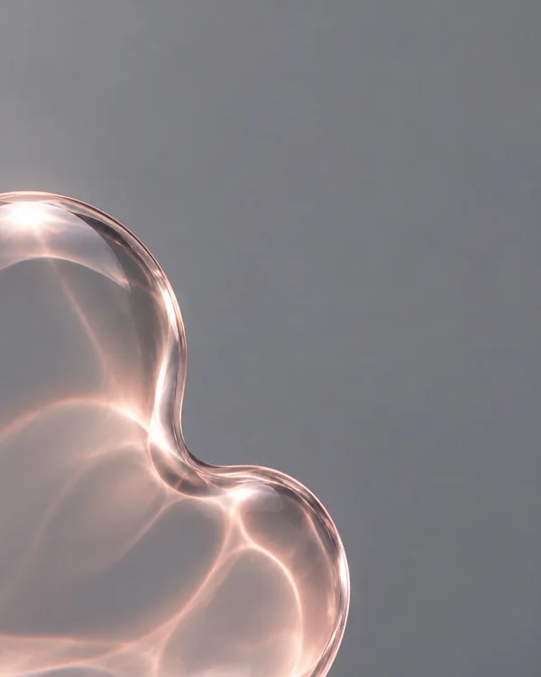 A large transparent, rose-tinted glass contour with two rounded lobes and a central indentation enters from the left and bottom edges against a smooth grey…