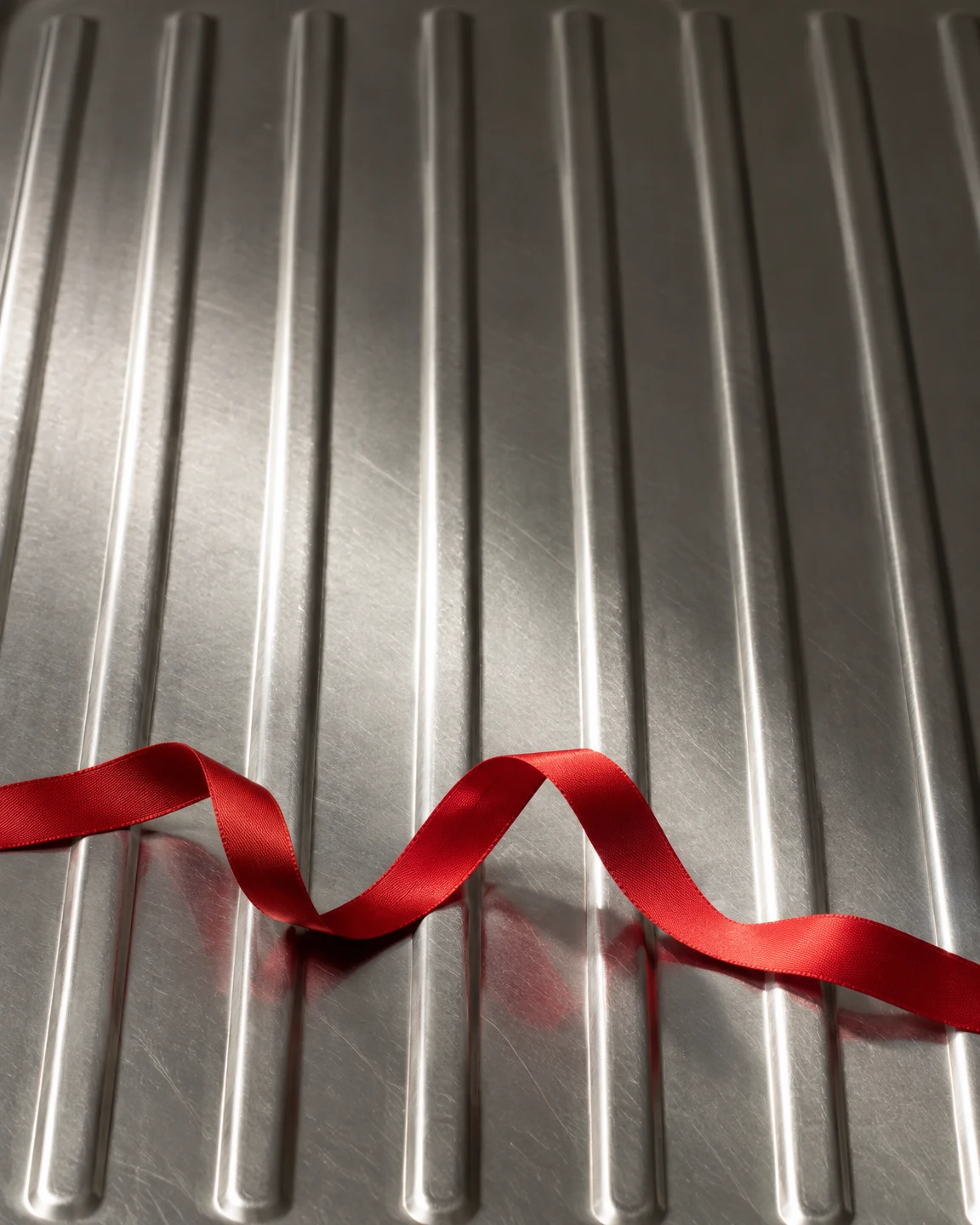 A loose red satin ribbon snakes across the lower third of a vertically ridged stainless-steel draining board, with reflections visible in the metal and open…