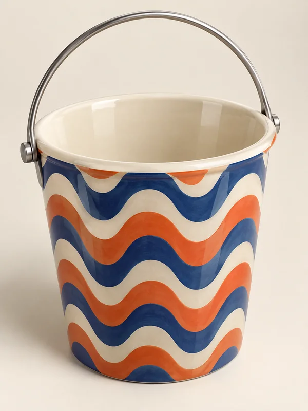 A glossy ivory ceramic bucket with a wide open rim and empty interior, decorated with broad cobalt-blue and coral-orange waves.