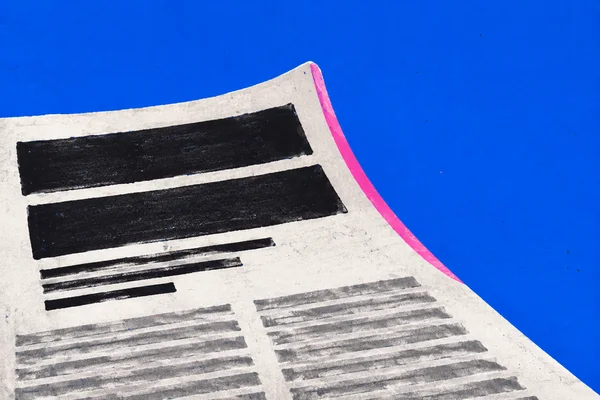 A close, oblique view of a white newspaper page with a curled edge and vivid pink strip against a cobalt-blue background.