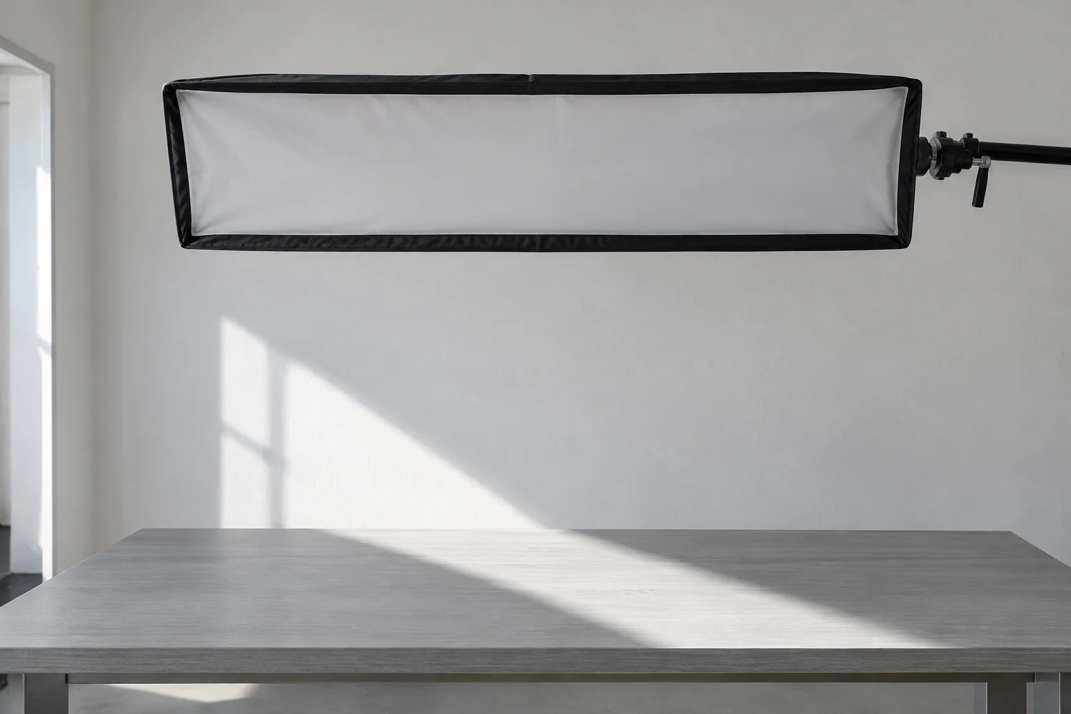 A long rectangular softbox hangs above an empty pale-grey desk, with its mounting hardware extending from the right.