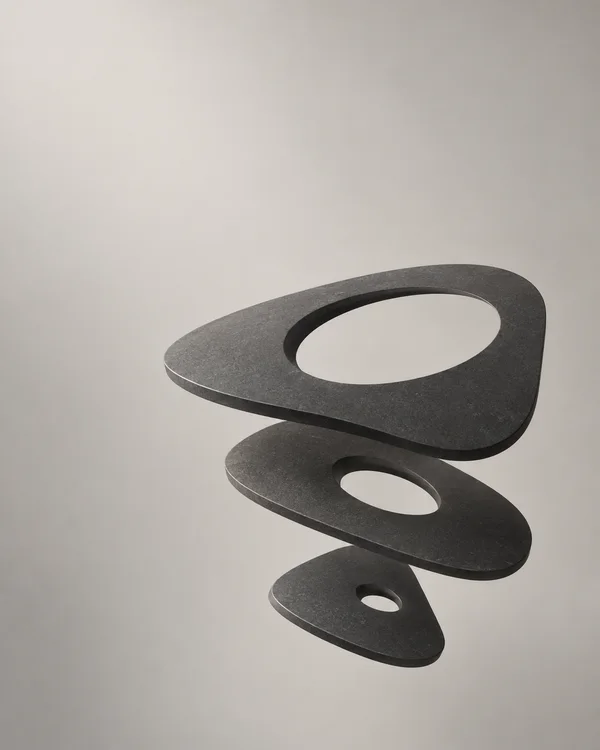 Three dark charcoal, gently curved slabs with oval openings float in a staggered vertical arrangement against a warm pale-grey background.