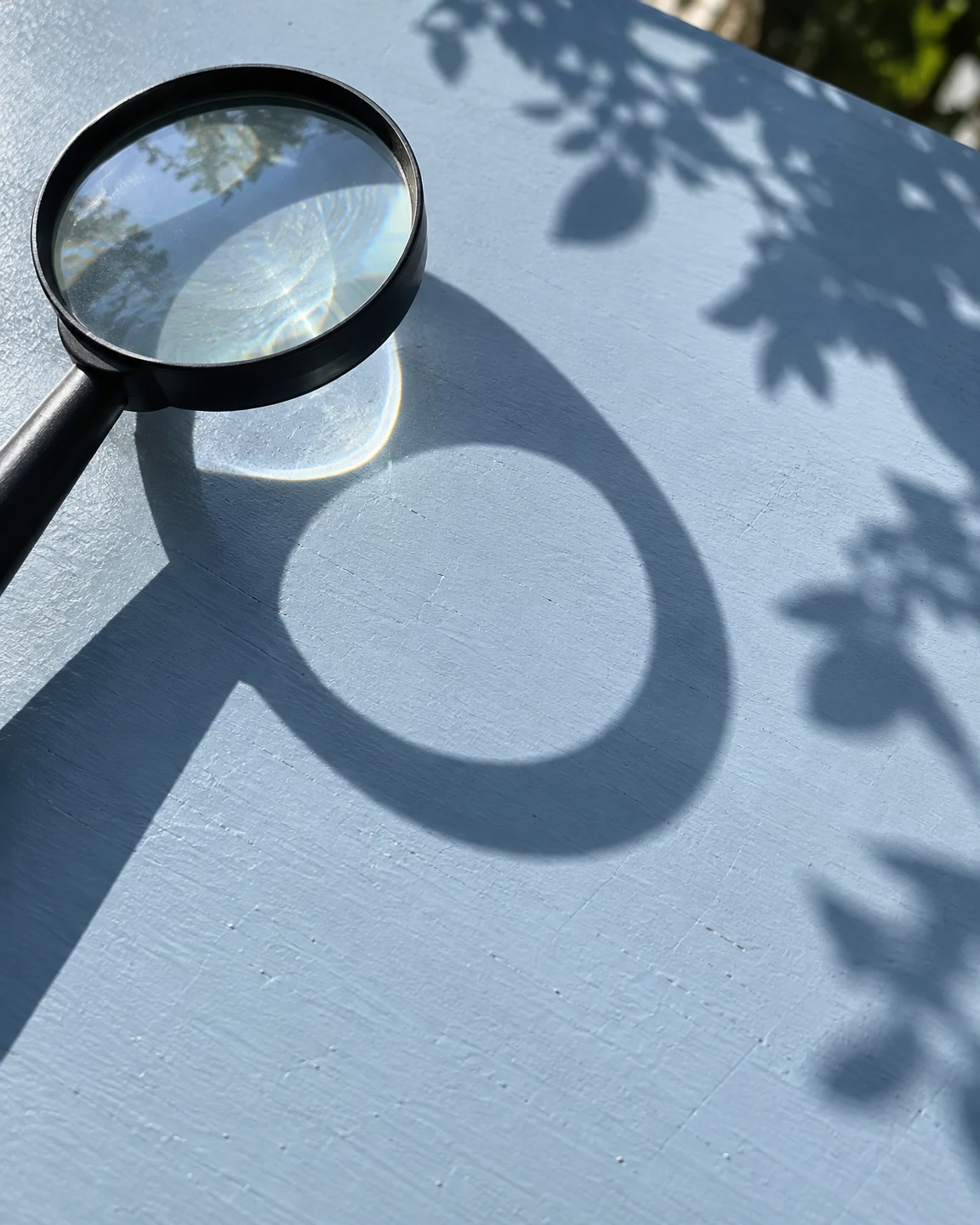 A black-handled magnifying glass rests partly cropped near the upper-left corner of a pale blue outdoor tabletop.