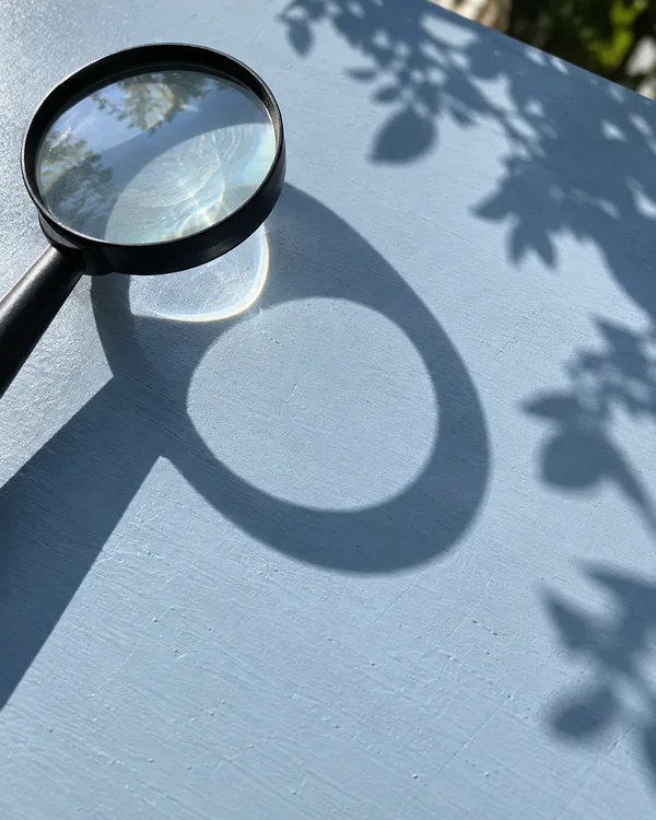 A black-handled magnifying glass rests partly cropped near the upper-left corner of a pale blue outdoor tabletop.