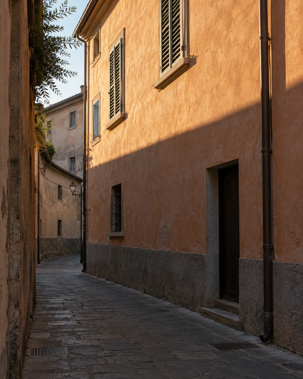 An empty narrow stone-paved lane bends between old plaster buildings.