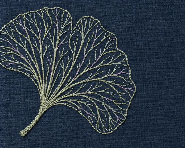 A large pale sage embroidered ginkgo leaf with lavender vein accents lies on dark midnight-blue linen, leaving open space on the right.