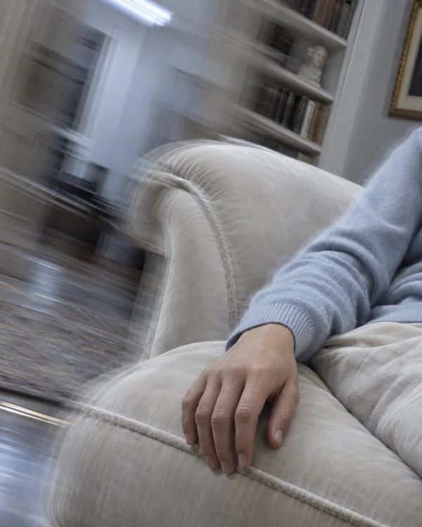 A relaxed hand rests on an ivory upholstered chaise, with a pale blue knit sleeve and a light-colored lap visible.