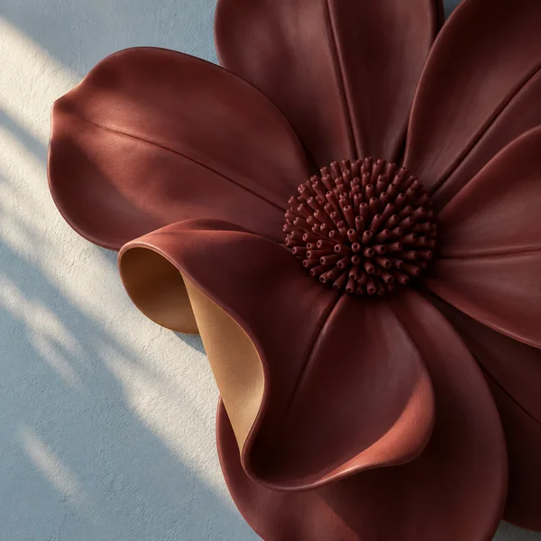 A large deep burgundy sculptural flower mounted on a pale blue textured wall, shown in close-up with a curled foreground petal exposing a caramel-colored…