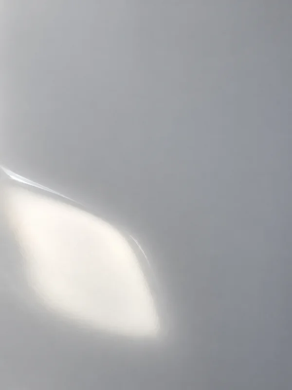 A softly glowing warm-white reflection with a narrow bright edge curves across the lower-left of a smooth silver-grey surface, leaving a broad field of quiet…