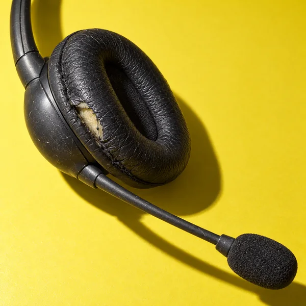 A worn charcoal single-ear support headset rests diagonally on a bright citron surface.