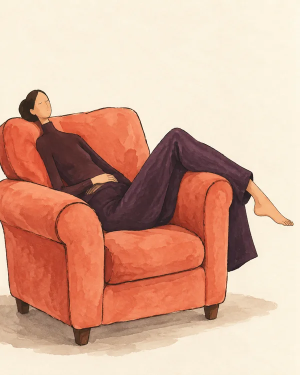 A dark-haired adult with closed eyes reclines sideways in a large coral armchair, wearing dark aubergine clothes; one bare foot extends to the right over the…
