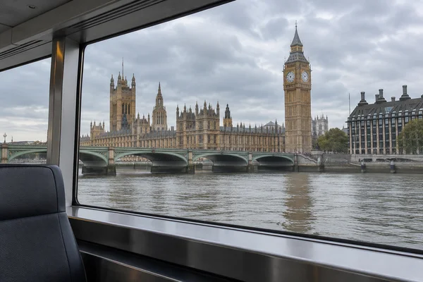 View of the Palace of Westminster and Elizabeth Tower across the Thames through a sightseeing boat’s panoramic window, with Westminster Bridge in the…