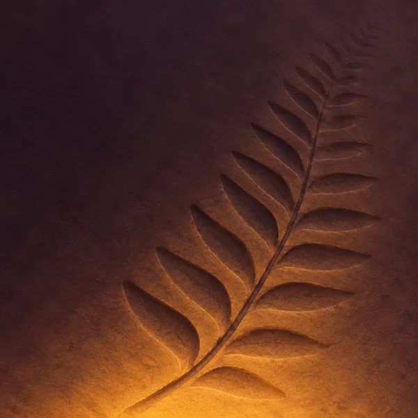A diagonal fern-like fossil impression with a slender curved stem and alternating tapered leaflets crosses a plum-colored textured surface, lit by an amber…