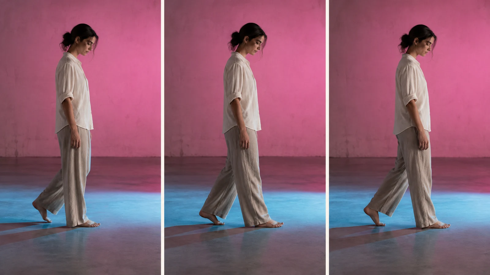 A barefoot woman in loose light trousers and an ivory shirt walks slowly in profile across a studio floor, shown in three side-by-side panels against a pink…