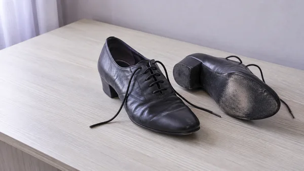 A pair of black leather lace-up ballroom shoes rests on a pale wood dressing table.