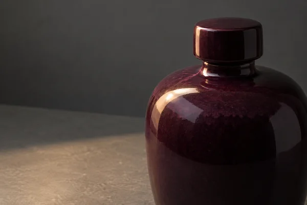 A glossy dark-plum ceramic bottle with a short stopper fills the right side of a close studio composition, its lower body cropped by the frame.