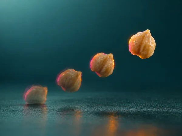 Four successive positions of a wrinkled beige chickpea rise diagonally from a teal surface, with the upper-right chickpea brightest and sharpest and…