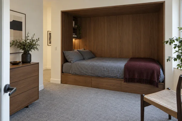 A low double bed with charcoal-grey bedding and a burgundy throw sits inside a walnut-lined rectangular alcove.