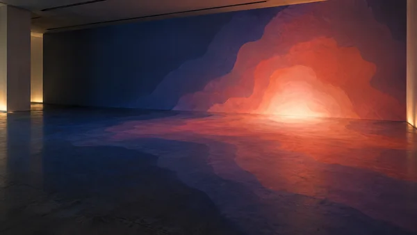 An empty contemporary gallery viewed obliquely, with a large irregular thermal-colour projection flowing across the plaster wall and concrete floor.